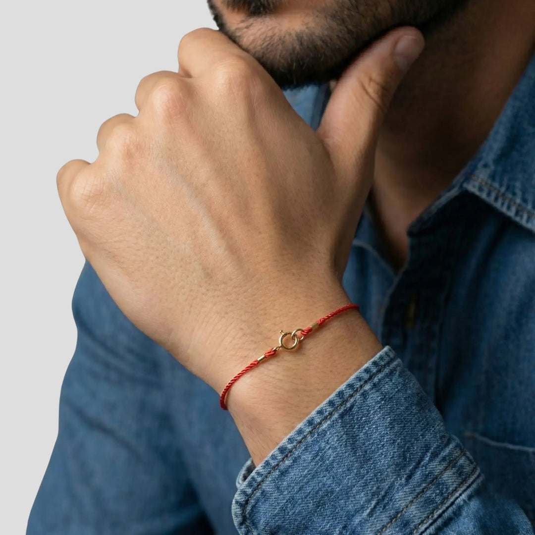 Person wearing a red string bracelet with a gold clasp on a plain background