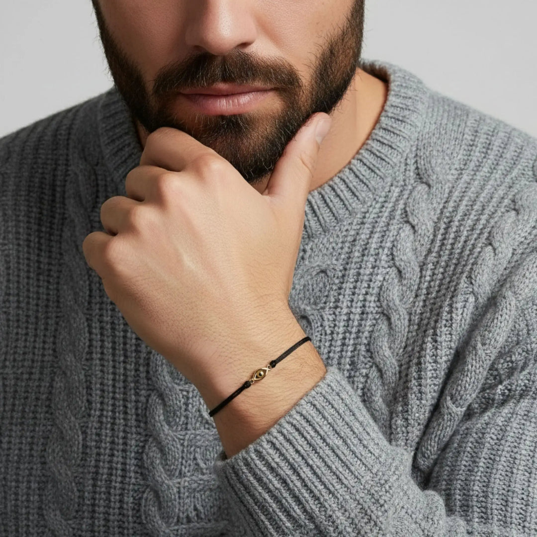 Man wearing a gray cable knit sweater with a gold evil eye red bracelet a close-up of his hand and bracelet.