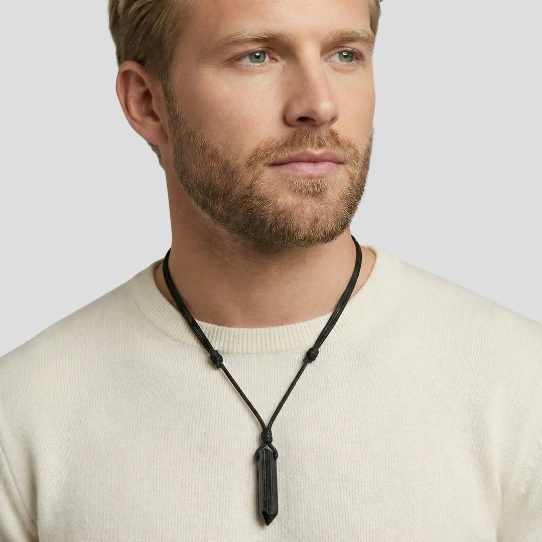 Man wearing a beige sweater with a black necklace against a light gray background
