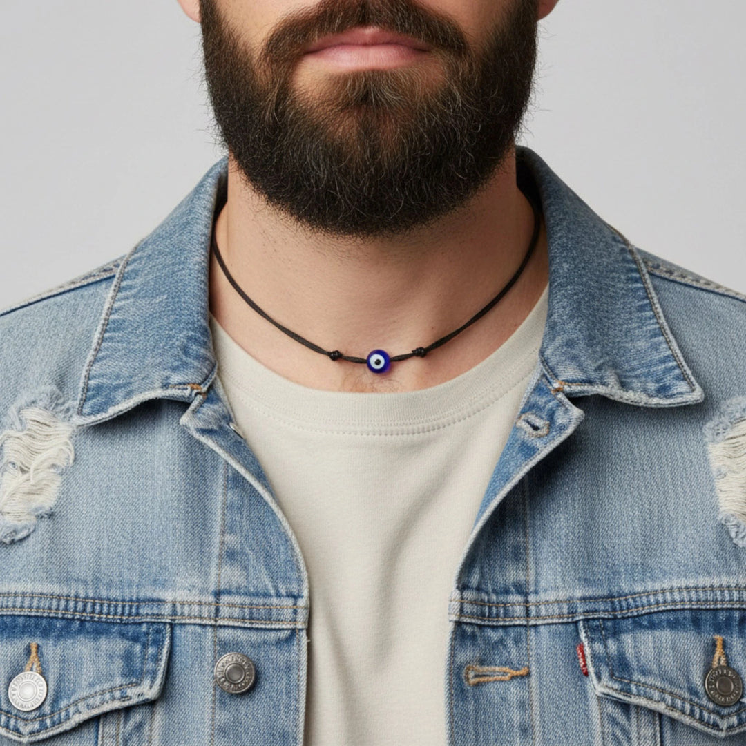 Man wearing a denim jacket with a necklace featuring an eye pendant.
