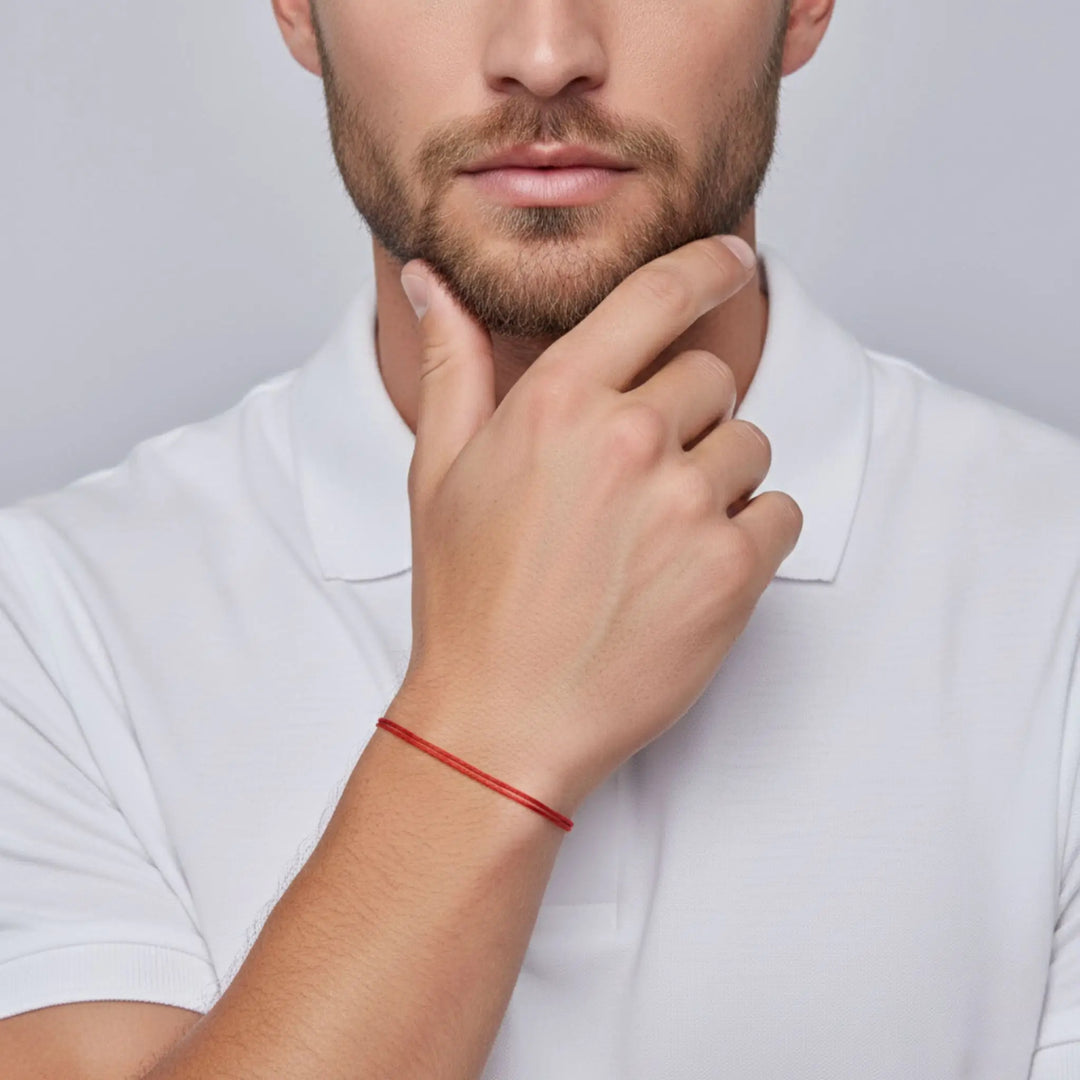 Man wearing a white shirt with a red bracelet on his wrist, against a plain background