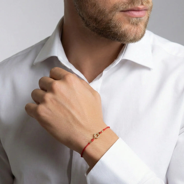 Man wearing a white shirt with a gold red bracelet on a plain background