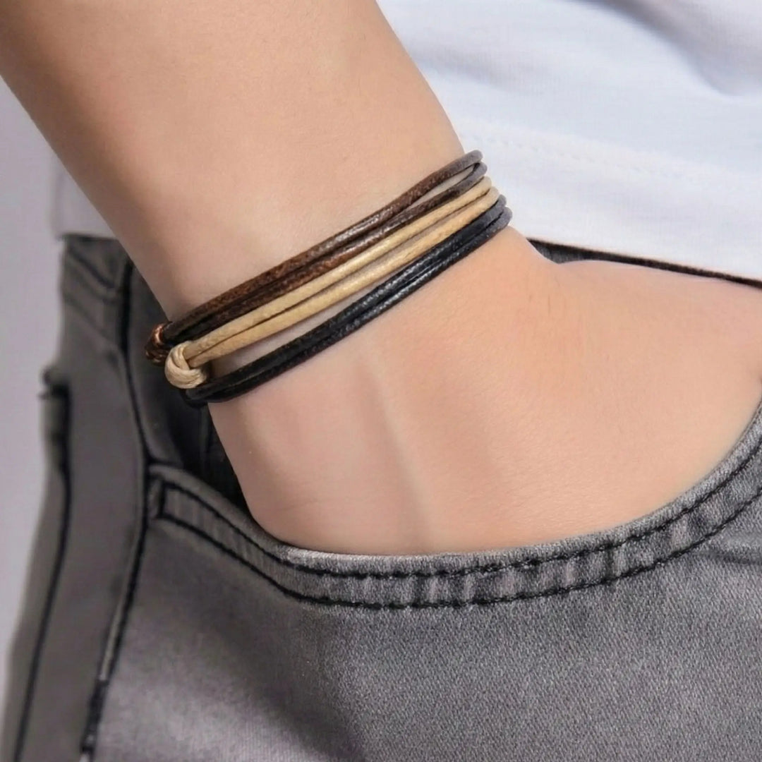 Close-up of a person's wrist wearing multiple faux leather bracelets on a neutral background
