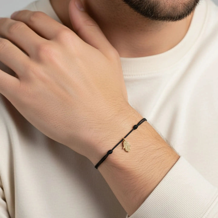 Person wearing a black gold hamsa bracelet with a gold charm on a neutral background