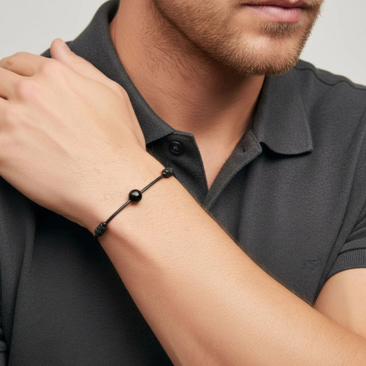 Man wearing a black tourmaline beaded bracelet on his wrist against a neutral background