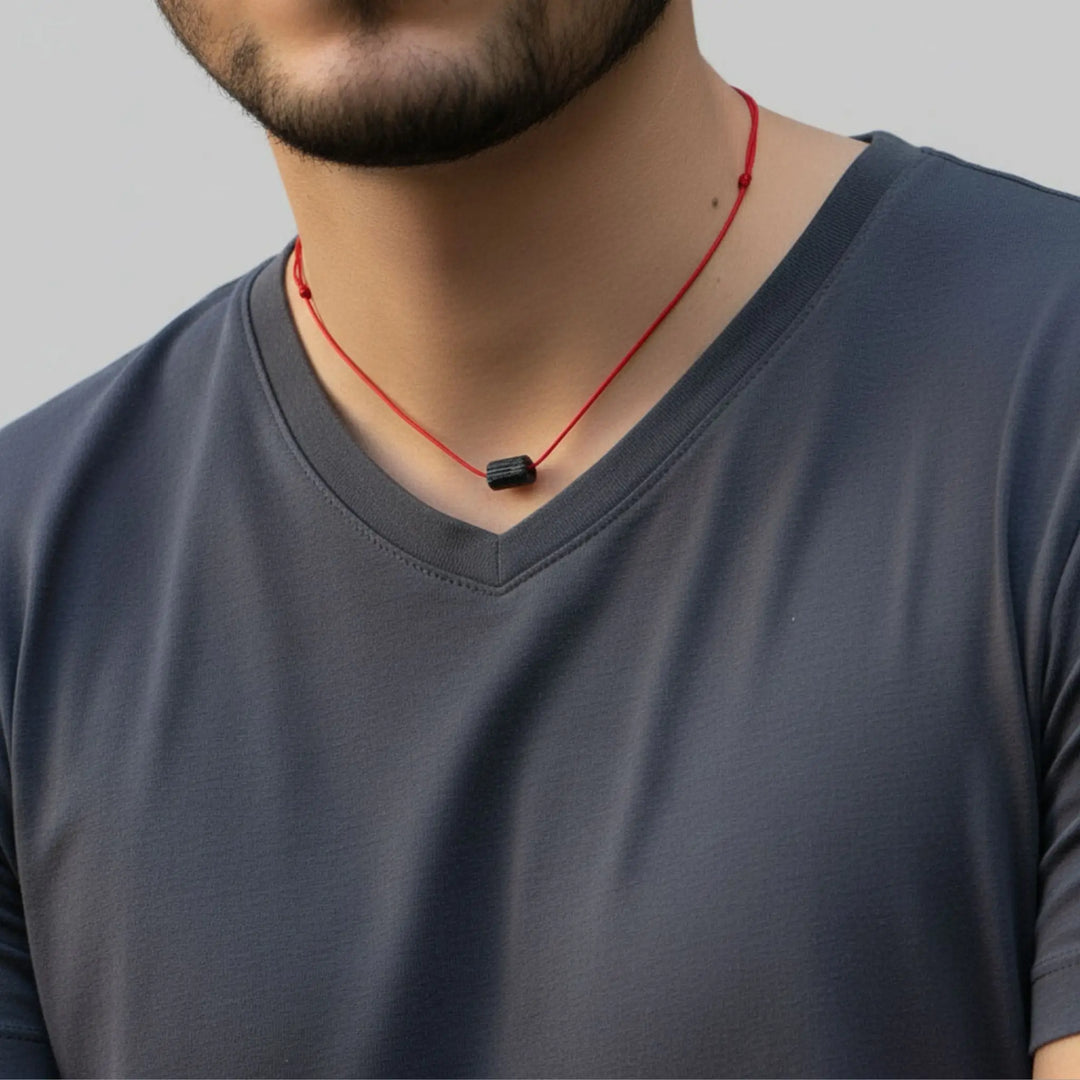 Man wearing a gray shirt with a red cord necklace featuring a black tourmaline pendant.