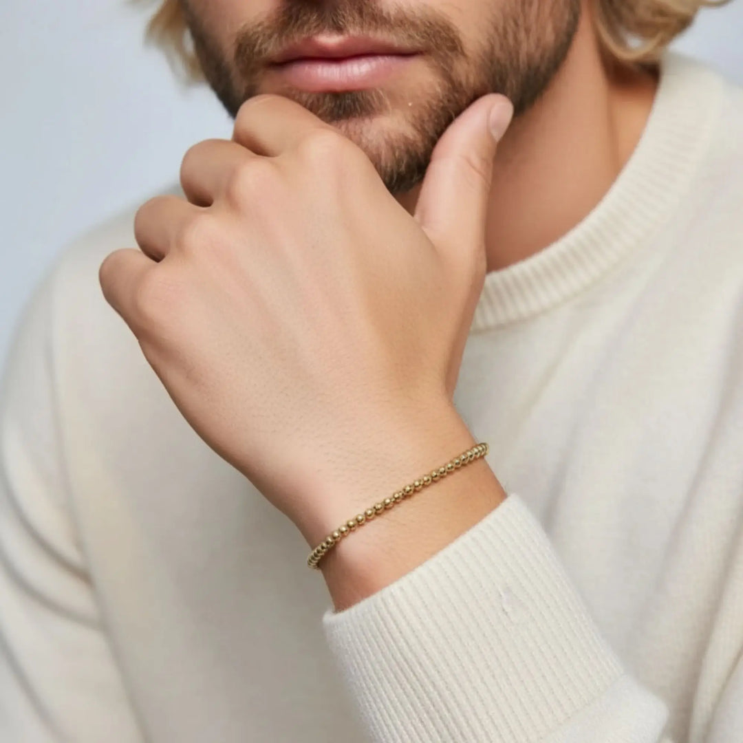 Close-up of a person wearing a gold bracelet on a plain background