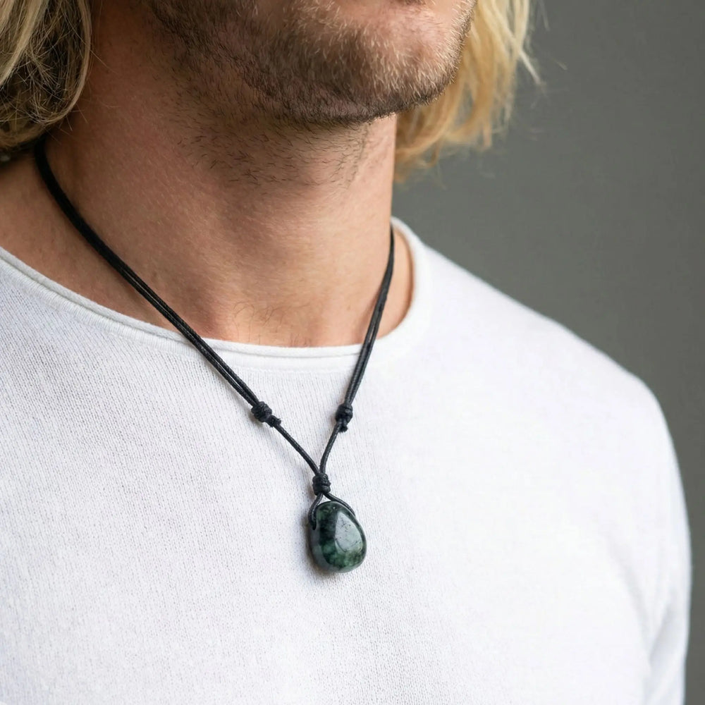 Man wearing a necklace with a green emerald pendant against a neutral background