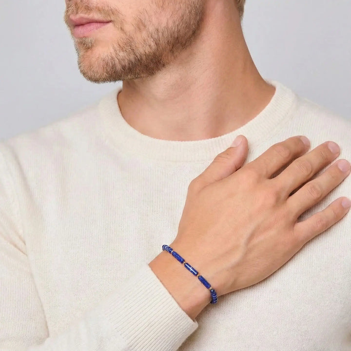 Man wearing a cream sweeter with a close-up of his hand and lapis lazuli bracelet on a light gray background