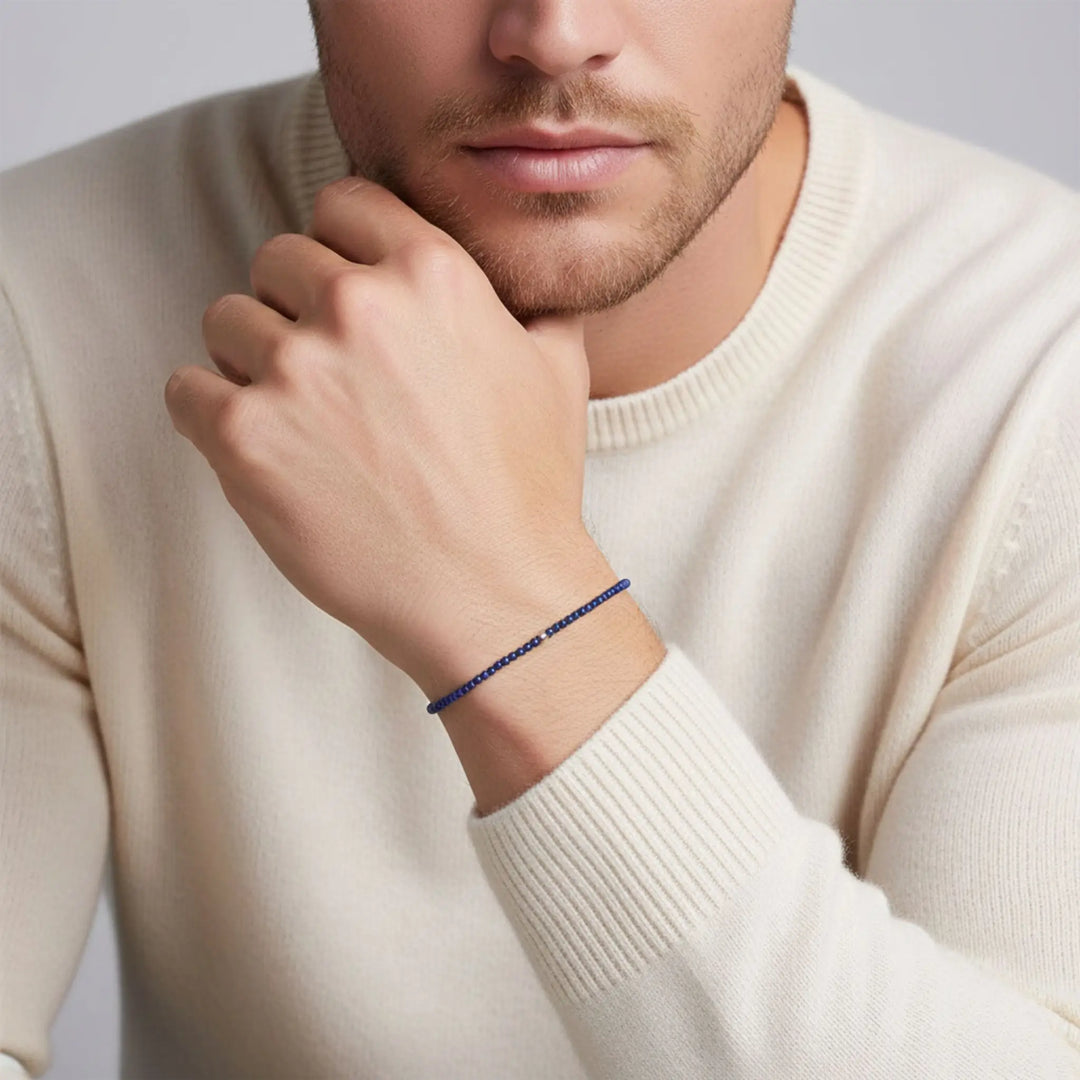 Man wearing a blue lapis lazuli beaded bracelet on his wrist, with a plain background
