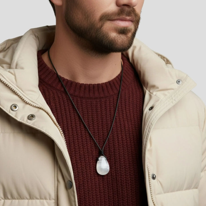 Man wearing a beige jacket and maroon sweater with a selenite  necklace featuring a large white stone.
