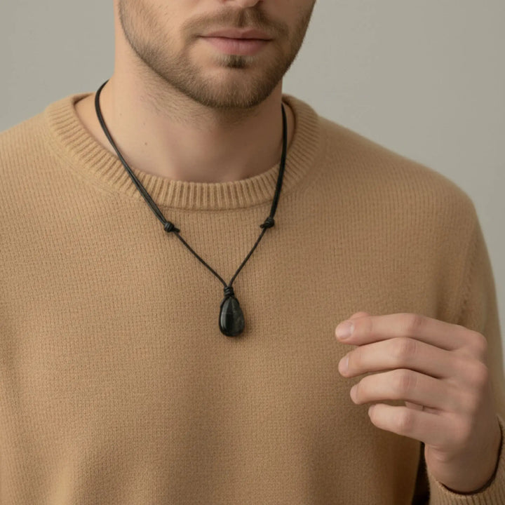 Man wearing a beige sweater with a black shungite necklace featuring a pendant.