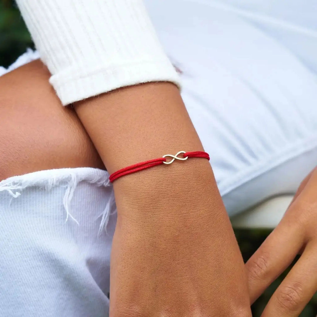 Red bracelet with a silver infinity symbol on a person's wrist.