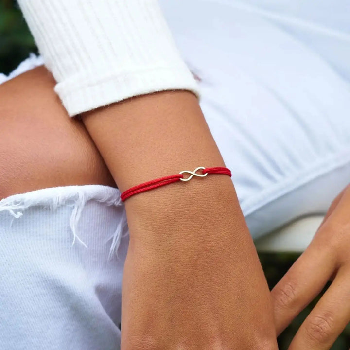 Red bracelet with a silver infinity symbol on a person's wrist.