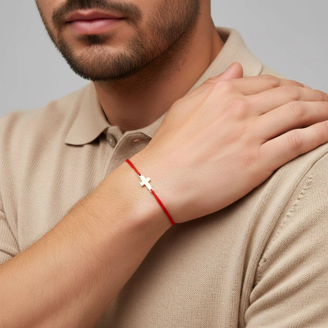 Man wearing a red bracelet with a small gold cross on a neutral background