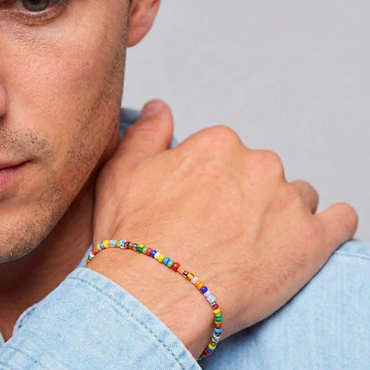 Man wearing a colorful beaded bracelet on a plain background