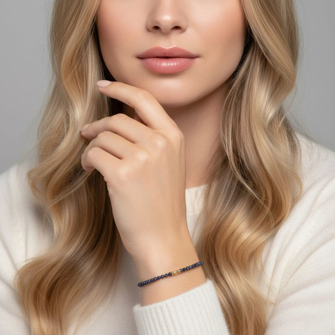 Woman with long blonde hair wearing a white sweater and a bracelet on a gray background