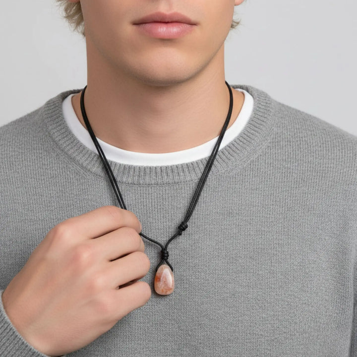 Person wearing a gray sweater holding a black necklace with a sunstone pendant.