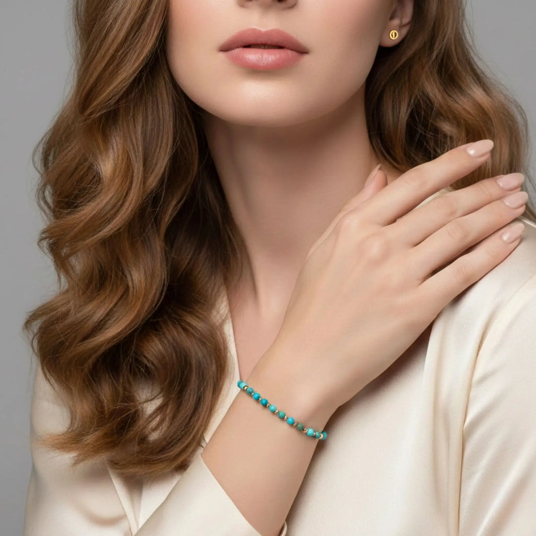 Woman wearing a turquoise beaded bracelet on a neutral background