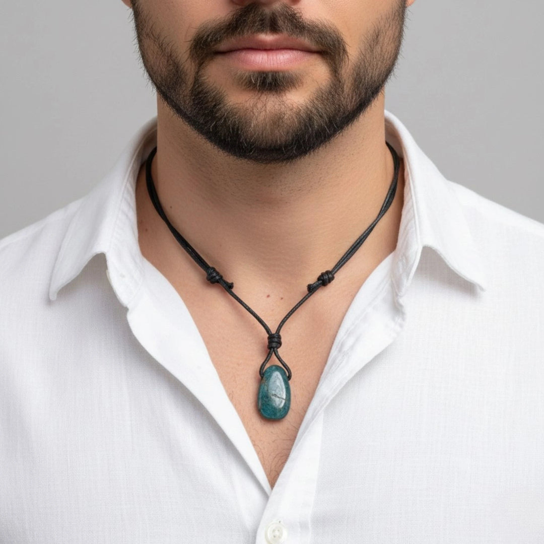Man wearing a white shirt with a black necklace featuring a green pendant against a gray background