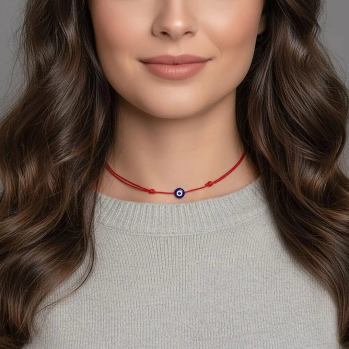 Woman wearing a red necklace with an evil eye pendant on a neutral background