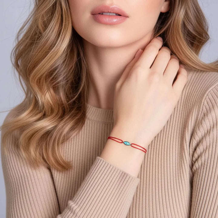 Woman wearing a red bracelet with a blue gemstone on a plain background