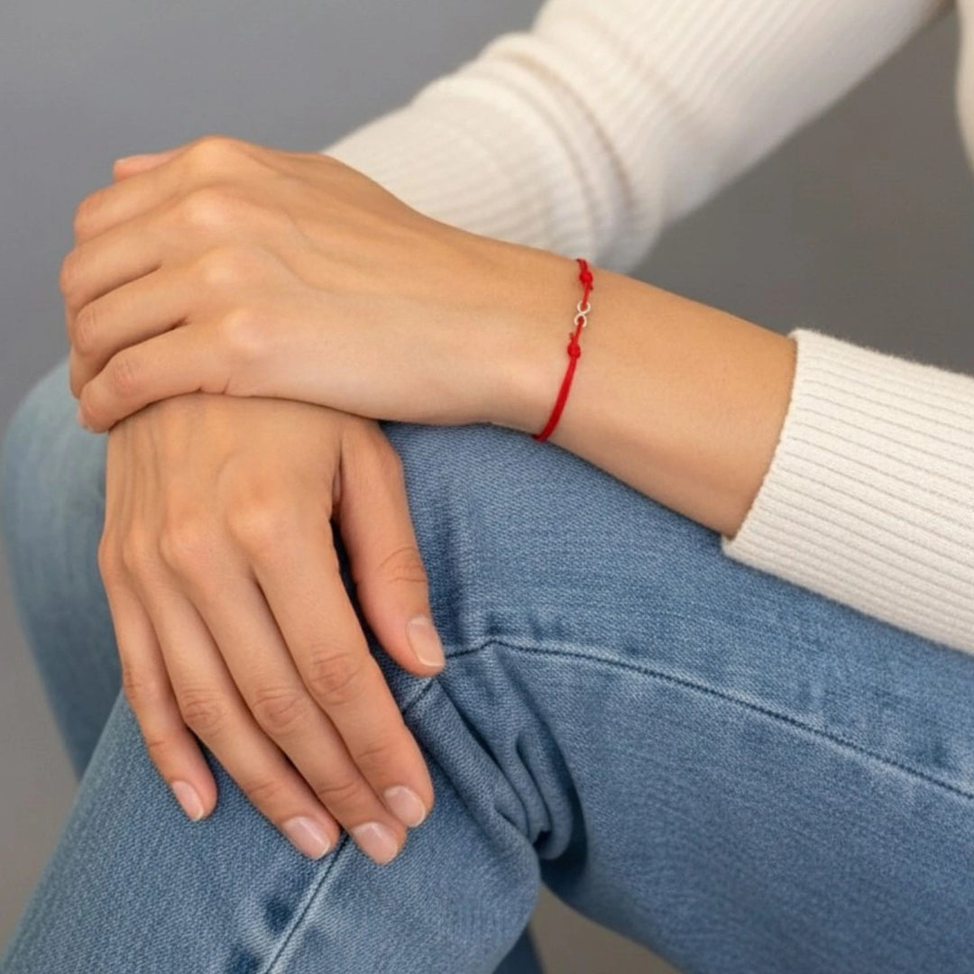 Person wearing a red bracelet with crossed arms on a gray background