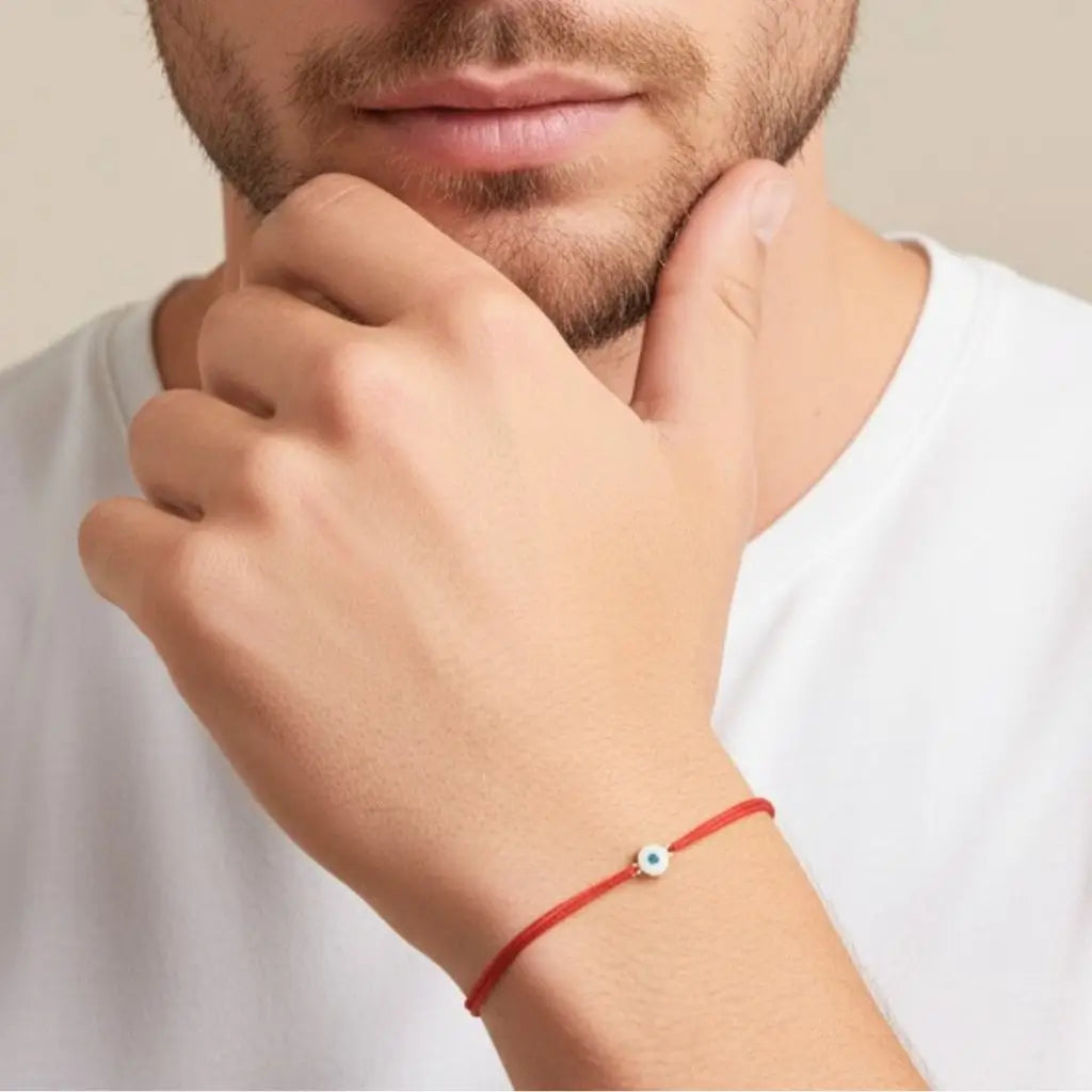 Close-up of a person wearing a red bracelet with a gold evil eye small bead, against a neutral background.