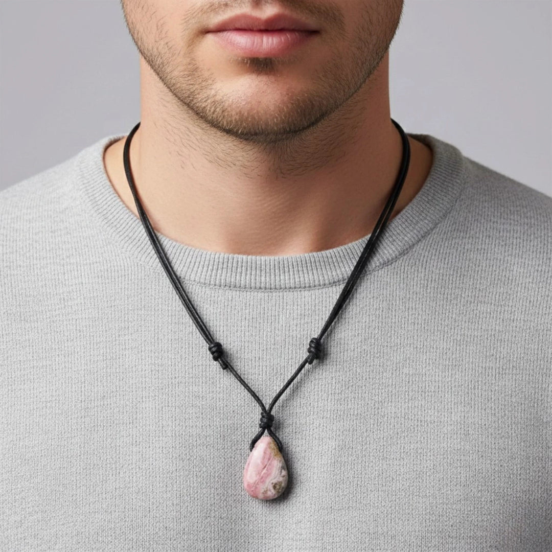 Man wearing a necklace with a pink stone rhodochrosite pendant against a gray background