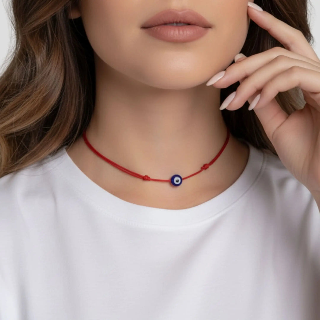 Woman wearing a red necklace with an evil eye pendant on a plain background