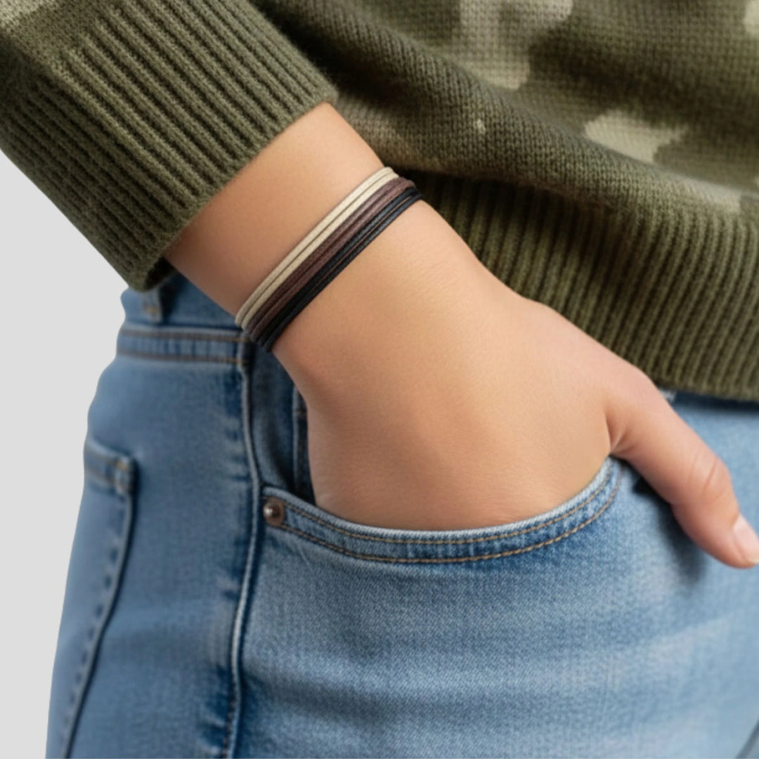 Person wearing a green sweater and blue jeans with a bracelet stack on a light gray background