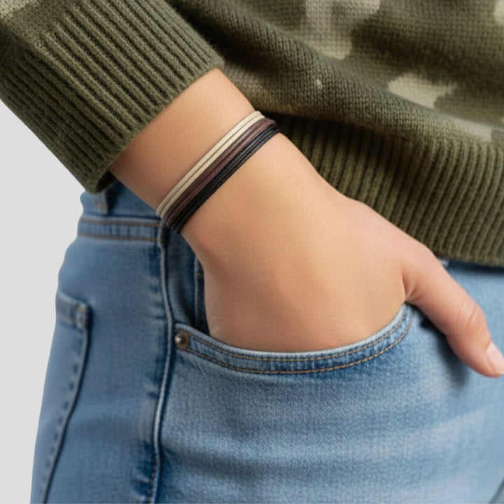 Person wearing a green sweater and blue jeans with a bracelet stack on a light gray background