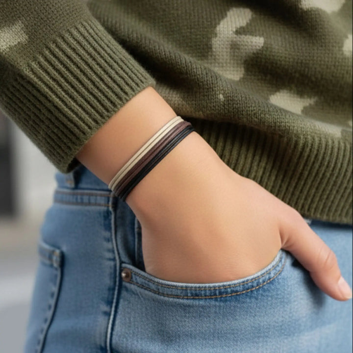 Person wearing a green sweater and blue jeans with a bracelet on a blurred background