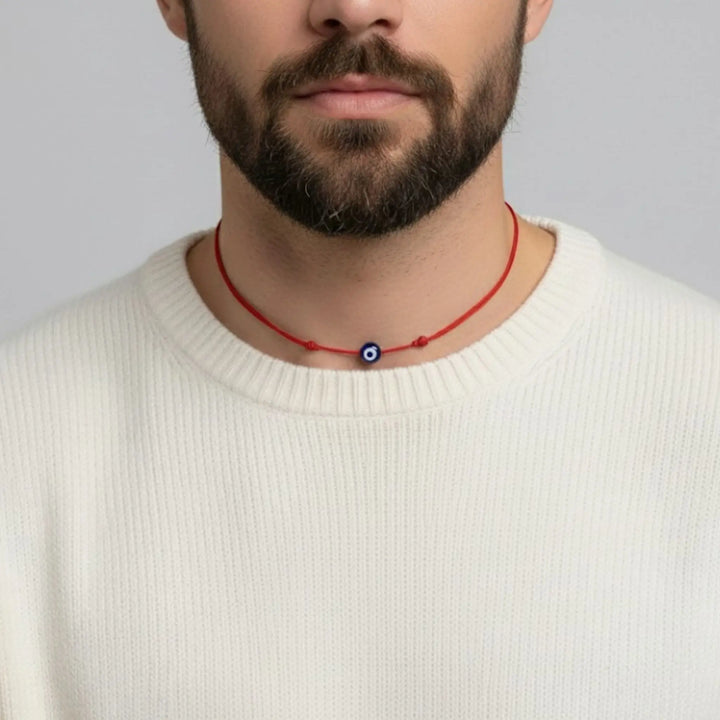 Man wearing a red string necklace with a blue evil eye bead against a gray background