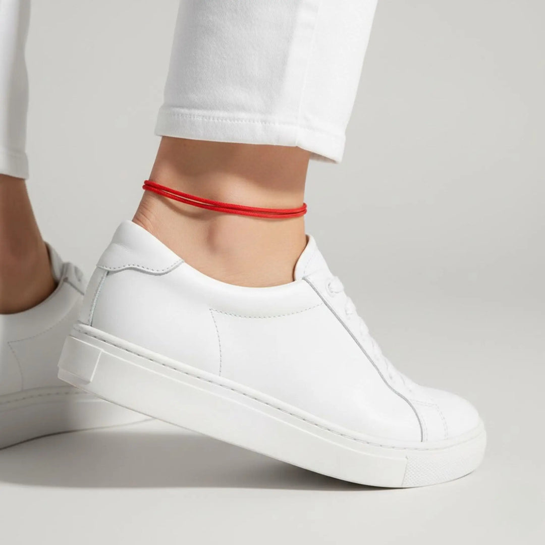 White sneakers worn with a red anklet on a light gray background