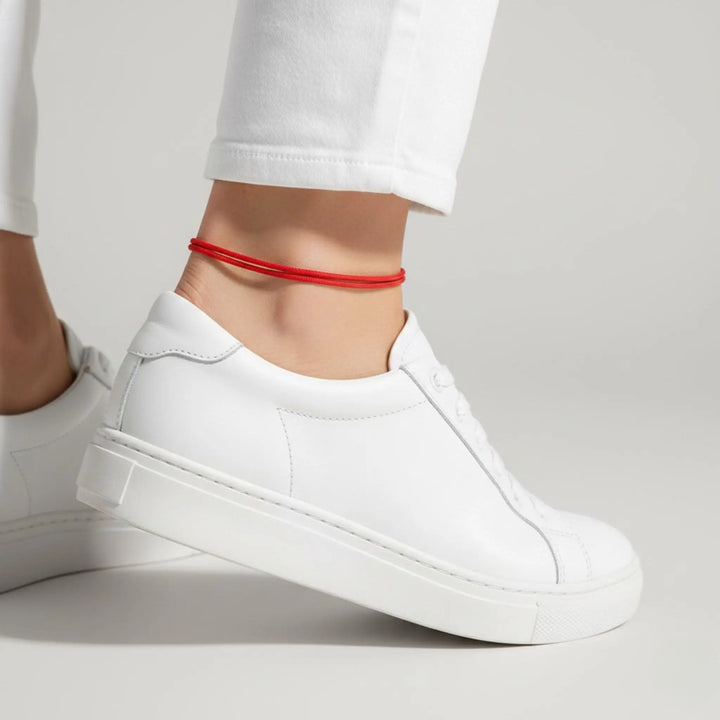 White sneakers worn with a red anklet on a light gray background