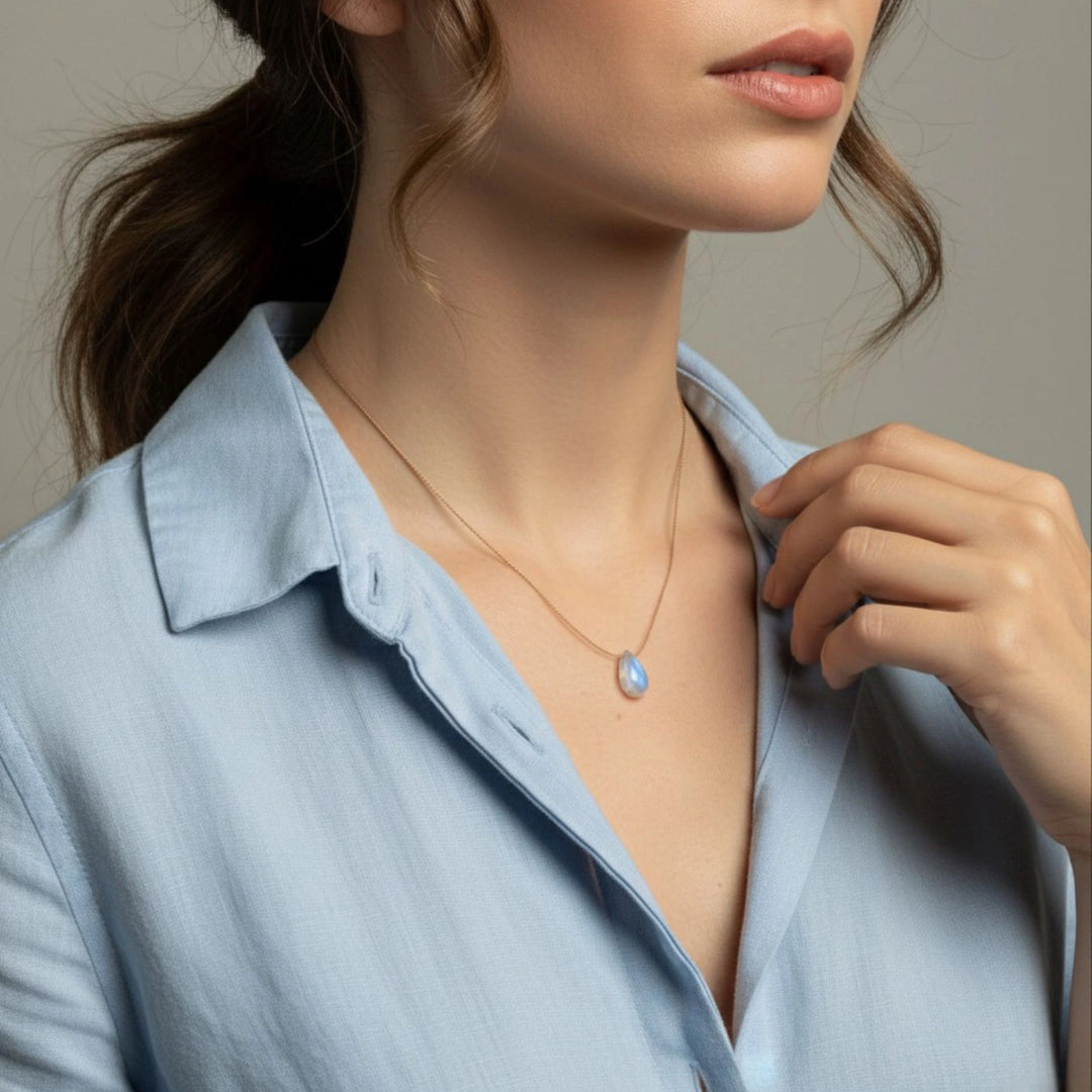 Woman wearing a light blue shirt with a delicate moonstone necklace against a neutral background