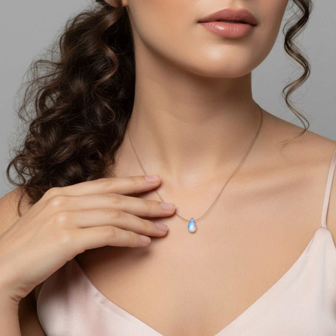 Woman wearing a necklace with a moonstone pendant against a neutral background