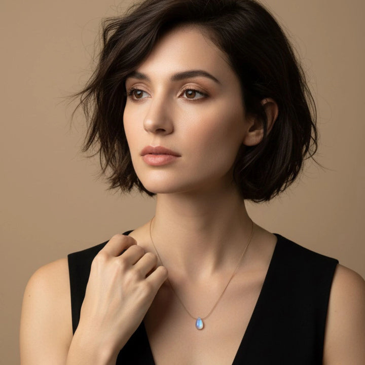 Woman wearing a necklace with a moonstone pendant against a beige background