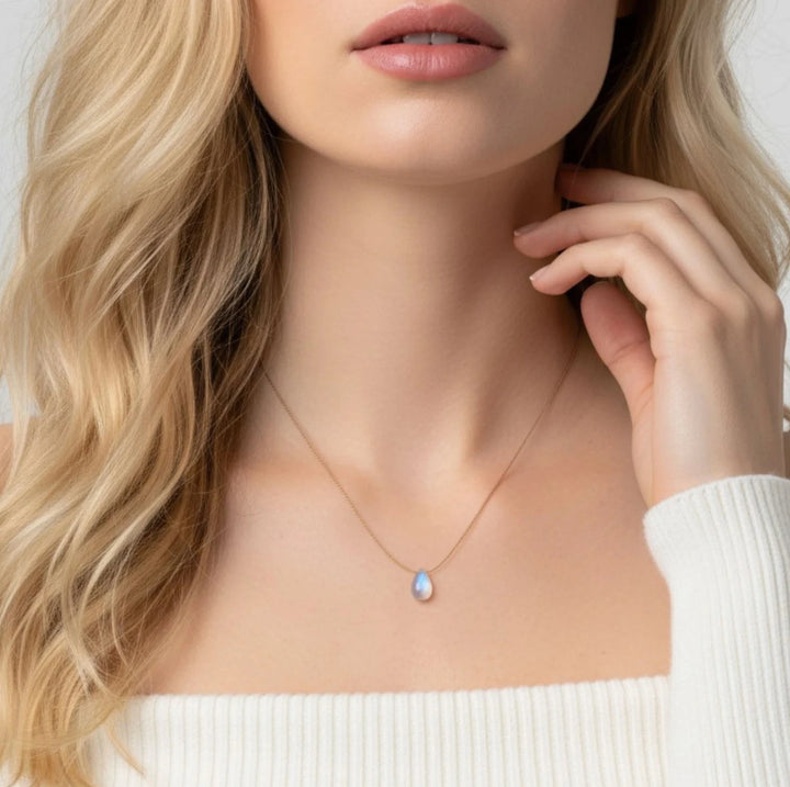 Close-up of a woman wearing a moonstone necklace with a pendant, against a neutral background.