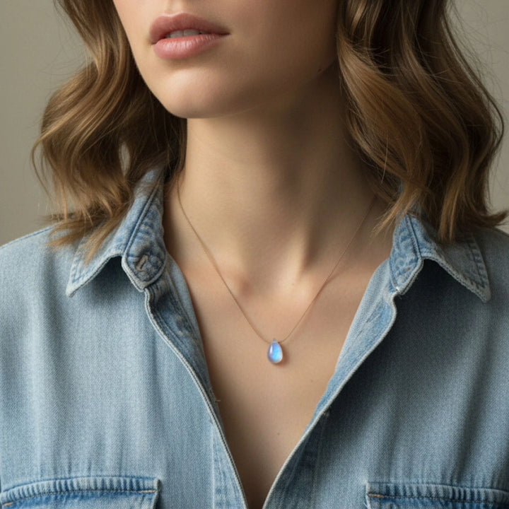 Necklace with a moonstone pendant worn by a person in a denim shirt.