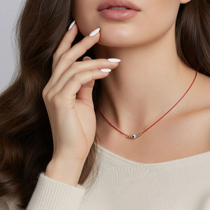 Close-up of a woman wearing a red necklace with small evil eye beads, against a neutral background.