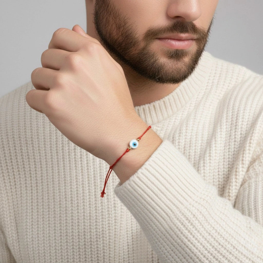 Man wearing a red string bracelet with a small bead on a plain background