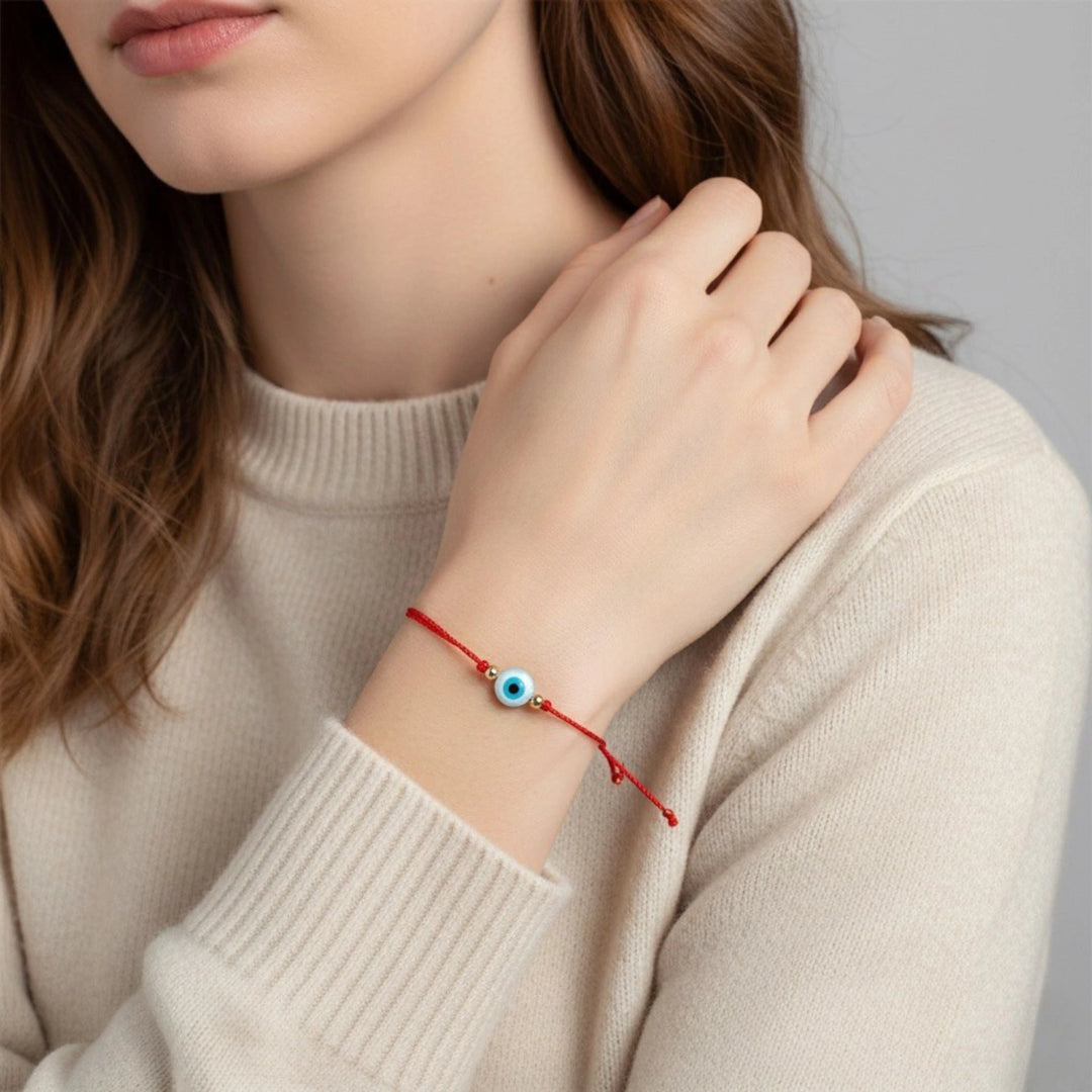 Person wearing a red bracelet with a blue evil eye charm on a neutral background