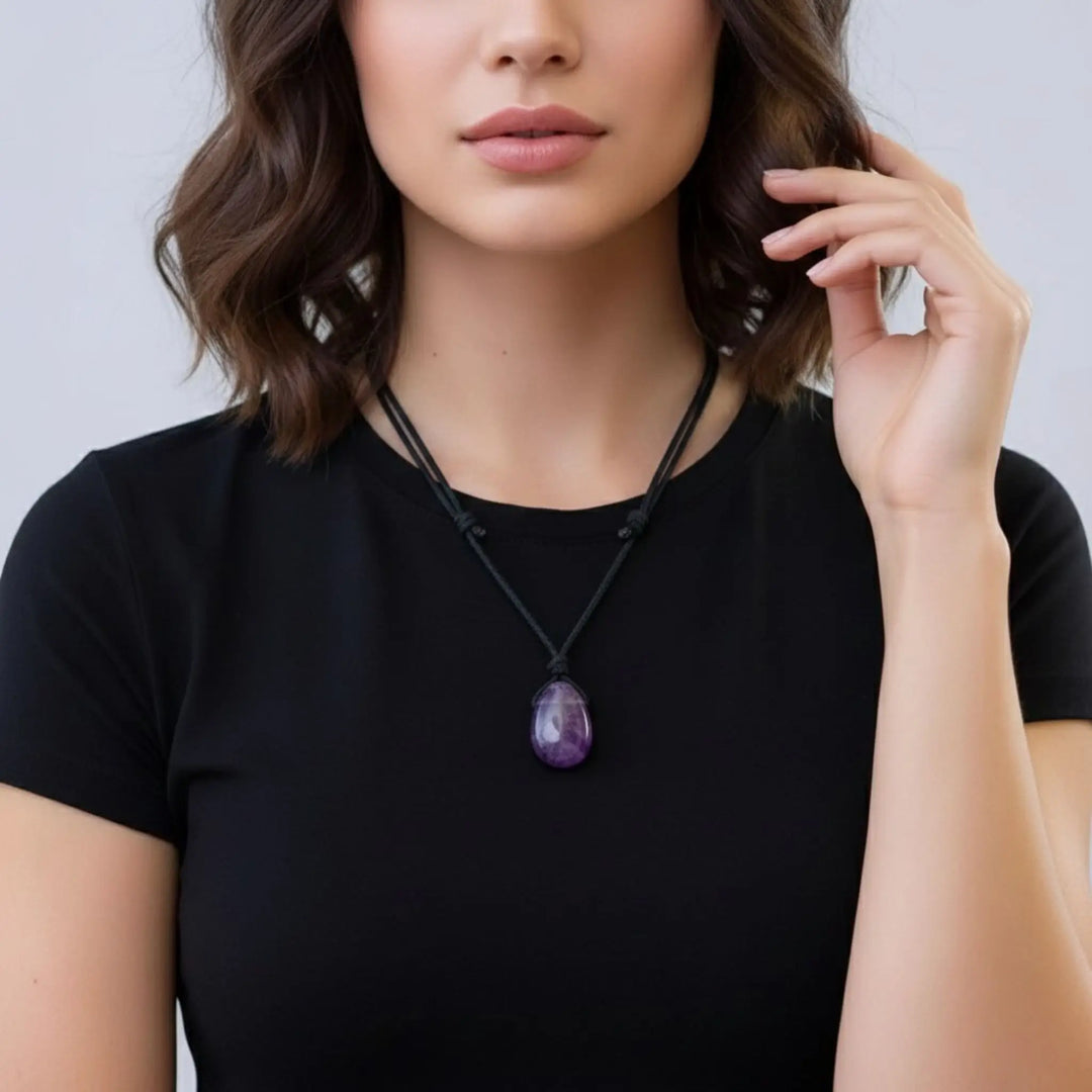 Woman wearing a black shirt with a purple pendant amethyst necklace against a plain background