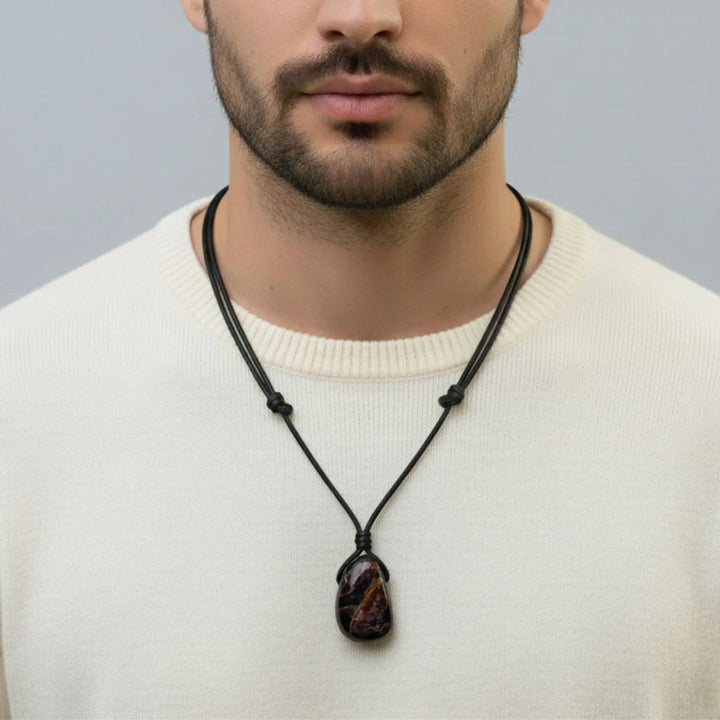Man wearing a necklace with a dark pendant against a neutral background