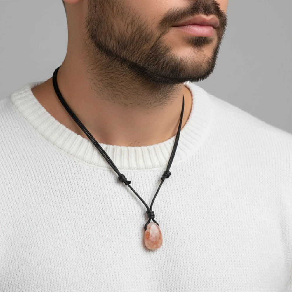 Man wearing a necklace with a sunstone pendant against a neutral background