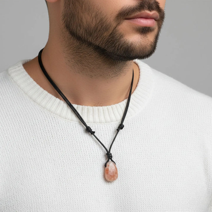 Man wearing a necklace with a sunstone pendant against a neutral background