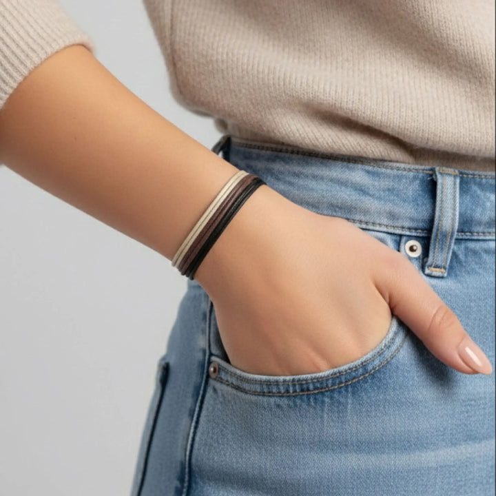 Person wearing a beige sweater and blue jeans with a bracelet on a light gray background