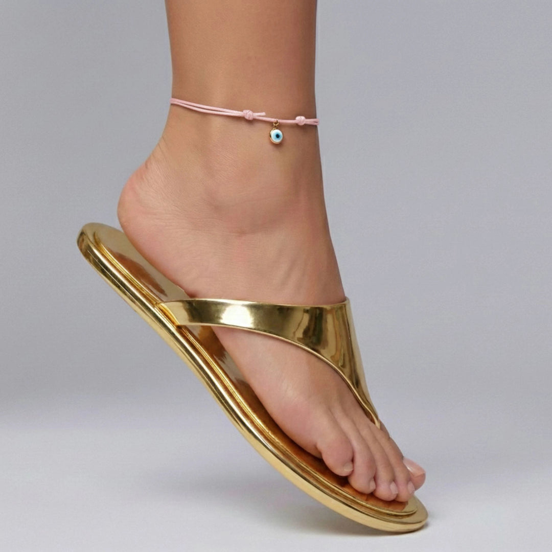 Gold sandal worn on a foot with a pink anklet against a gray background